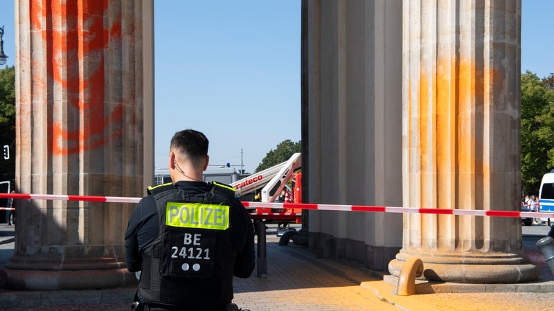 Polizisten stehen am Brandenburger Tor, das Mitglieder der Klimaschutzgruppe Letzte Generation am Sonntagvormittag mit oranger Farbe angesprüht haben. Die Polizei nahm nach eigenen Angaben 13 Mitglieder vor Ort fest.