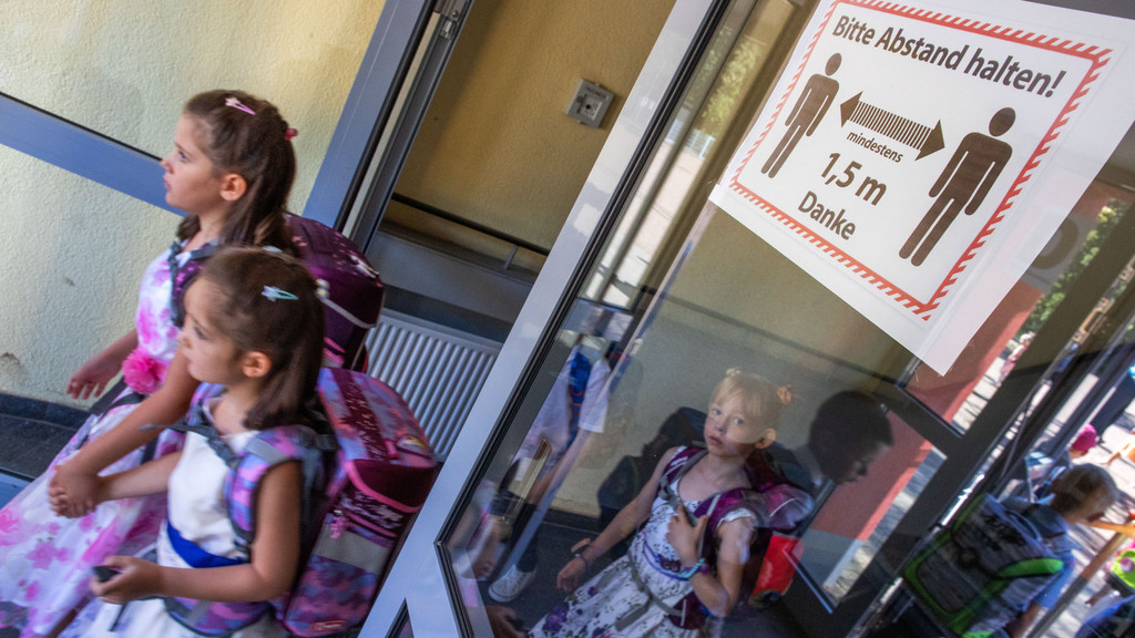 Schulkinder gehen durch eine Glastür, auf der ein Sicherheitshinweis zum Abstand halten steht.