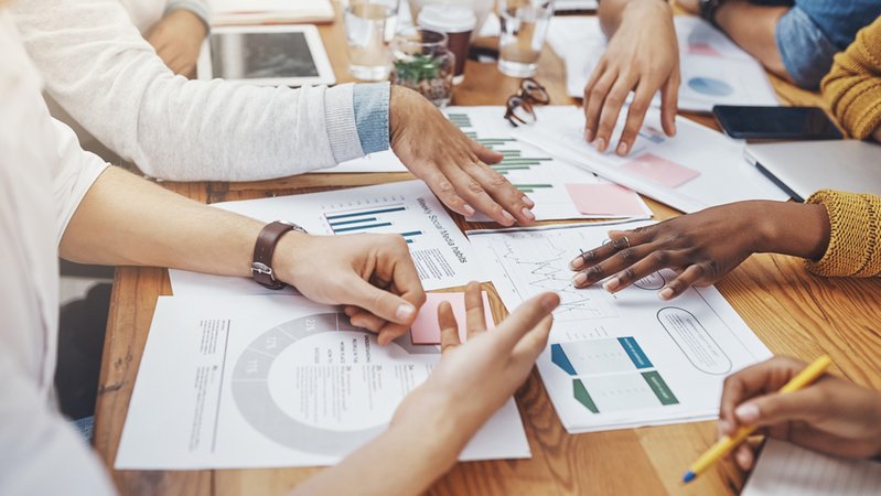 Mehrere Menschen diskutieren an einem Tisch über verschiedene Daten und Statistiken, die vor ihnen liegen | Bild: stock.adobe.com/BestCam/peopleimages.com Mehrere Menschen diskutieren an einem Tisch über verschiedene Daten und Statistiken, die vor ihnen liegen