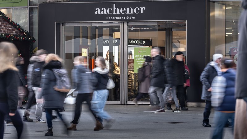 Menschen laufen am Eingang zum Modegeschäft Aachener vorbei.