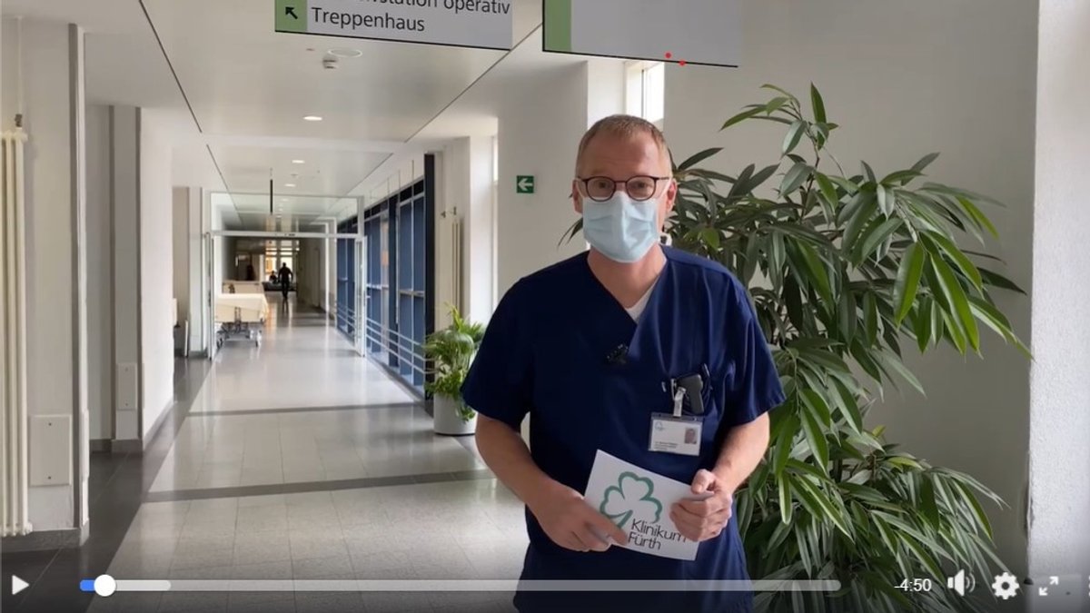Screenshot eines Videos. Es zeigt den Pandemiebeauftragten Manfred Wagner im blauen Arztkittel in einem Flur des Klinikums Fürth.