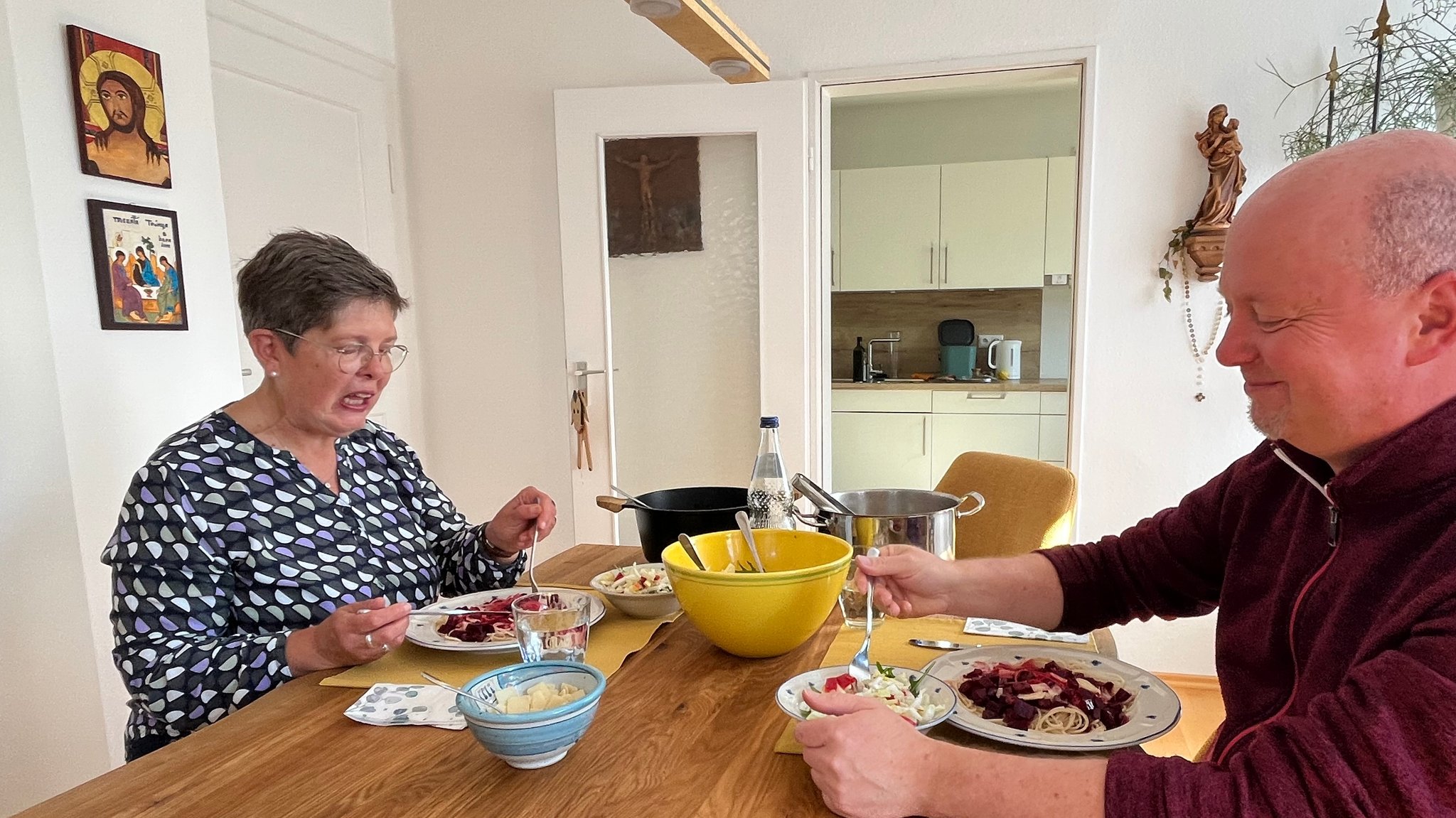 Petra Miller und der Pfarrer Michael Kratschmer essen an einem Tisch Spaghetti und Salat.