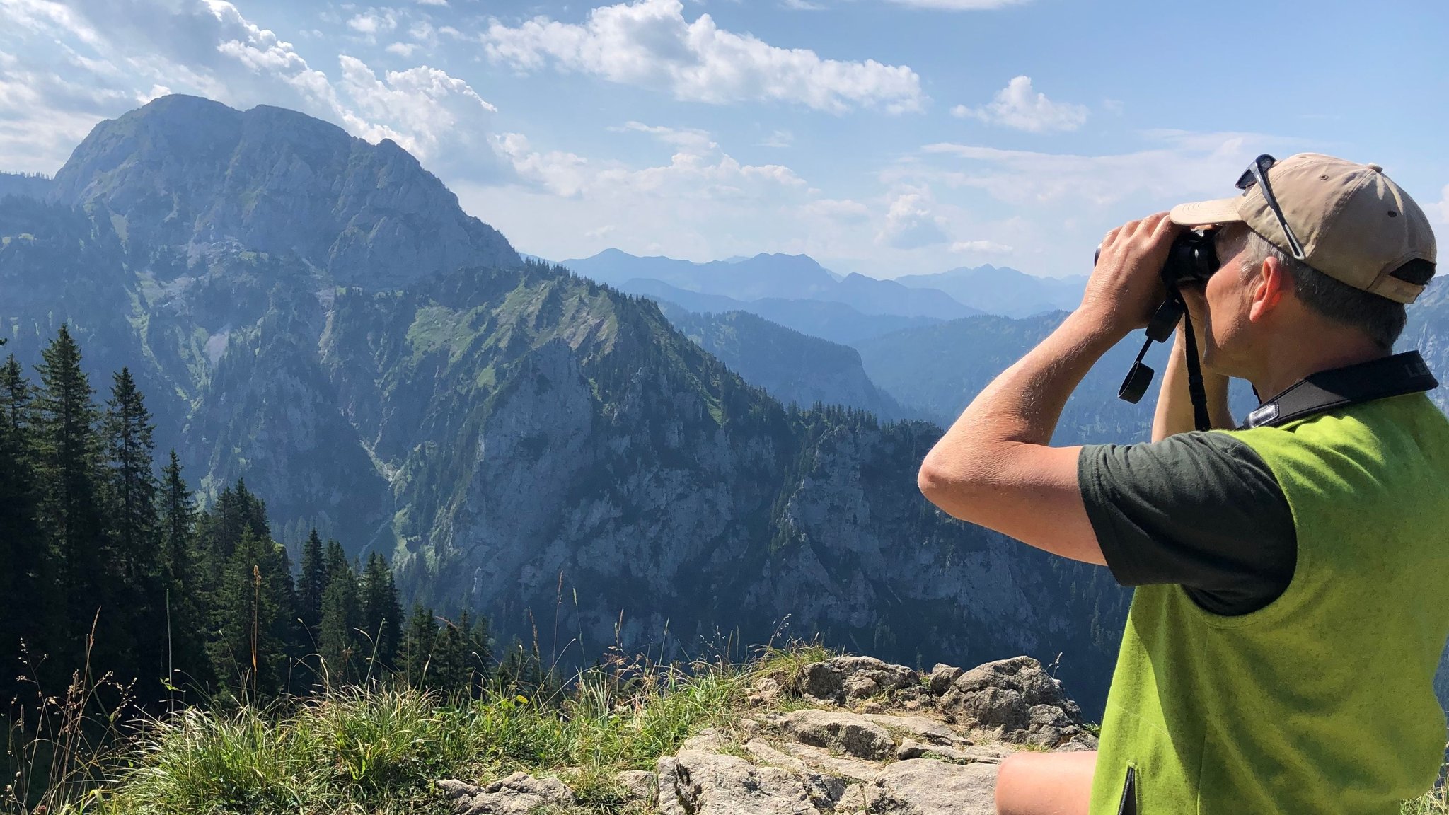 Gebietsbetreuer Tom Hennemann blickt mit dem Fernglas vom Tegelberg aus in die Berge.