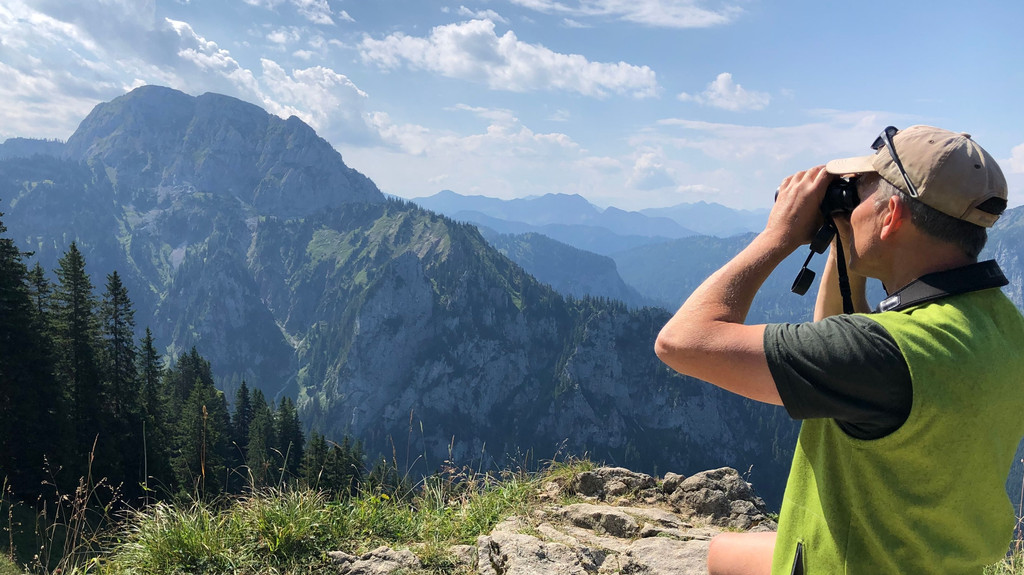 Gebietsbetreuer Tom Hennemann blickt mit dem Fernglas vom Tegelberg aus in die Berge.