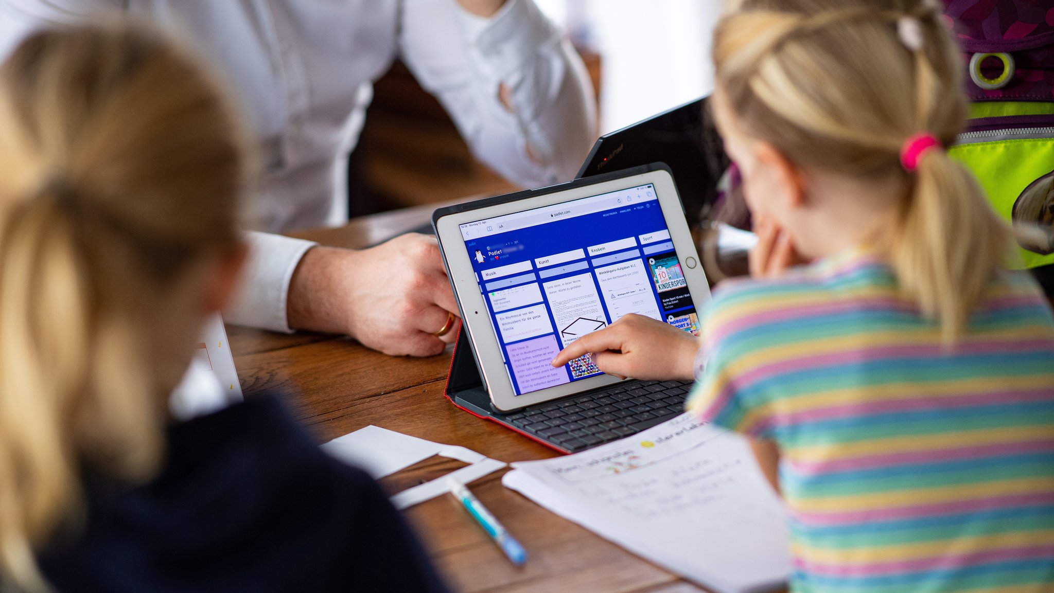 Eine 7-jährige Erstklässlerin (r) und eine 9jährige Viertklässlerin sitzen vor einem iPad und lernen im Homeschooling für die Schule. 