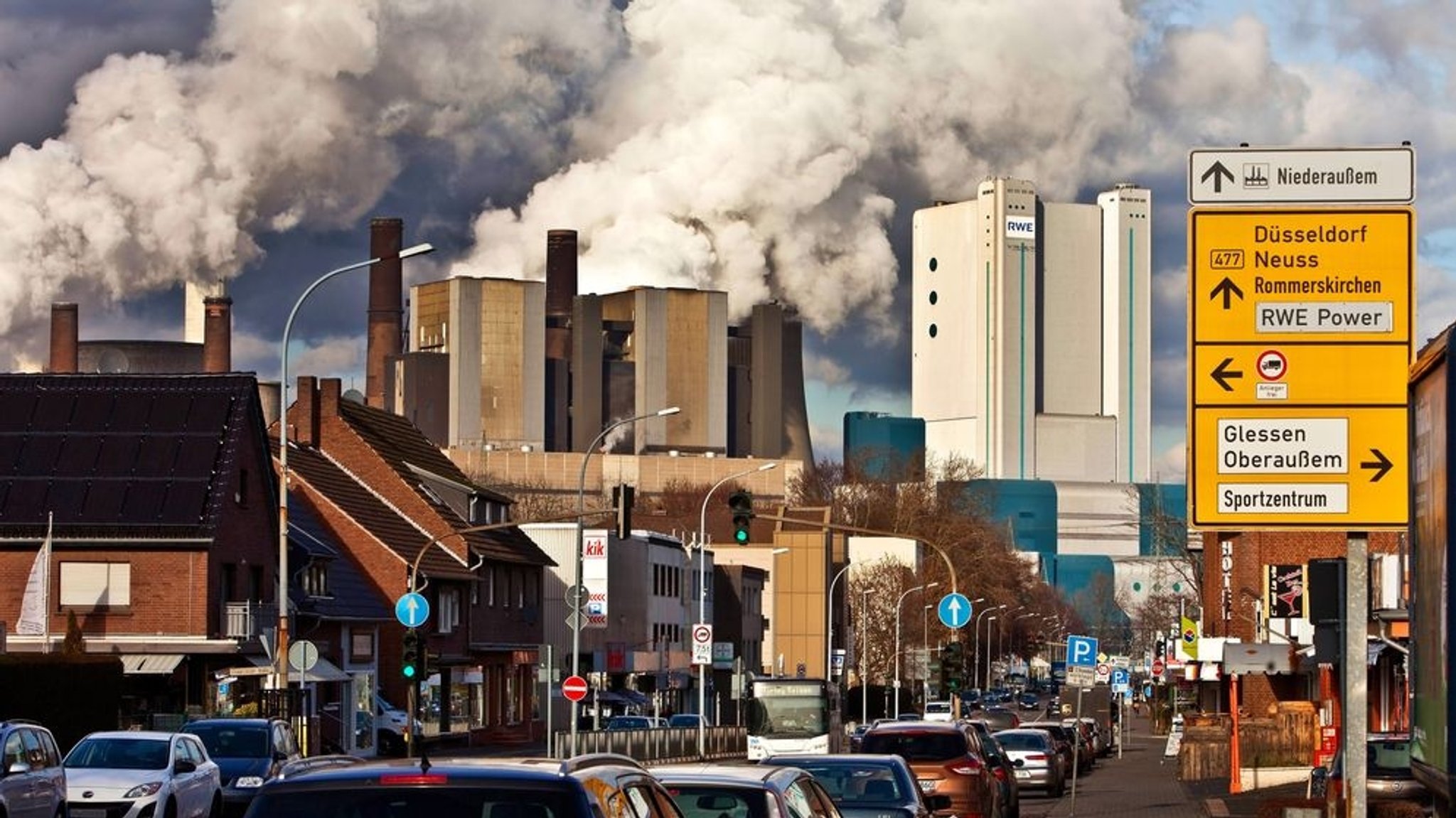 Eine Straße in Niederaußem mit Braunkohlekraftwerk im Hintergrund.