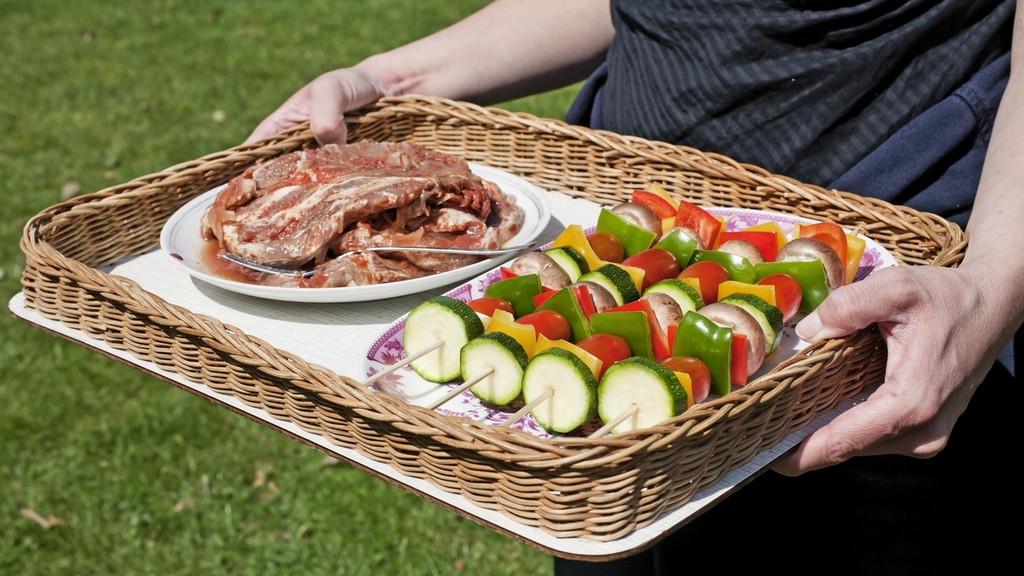 Eine Frau trägt ein Tablett mit Gemüsespießen und mariniertem Schweinefleisch | Bild: picture alliance / dpa Themendienst Eine Frau trägt ein Tablett mit Gemüsespießen und mariniertem Schweinefleisch