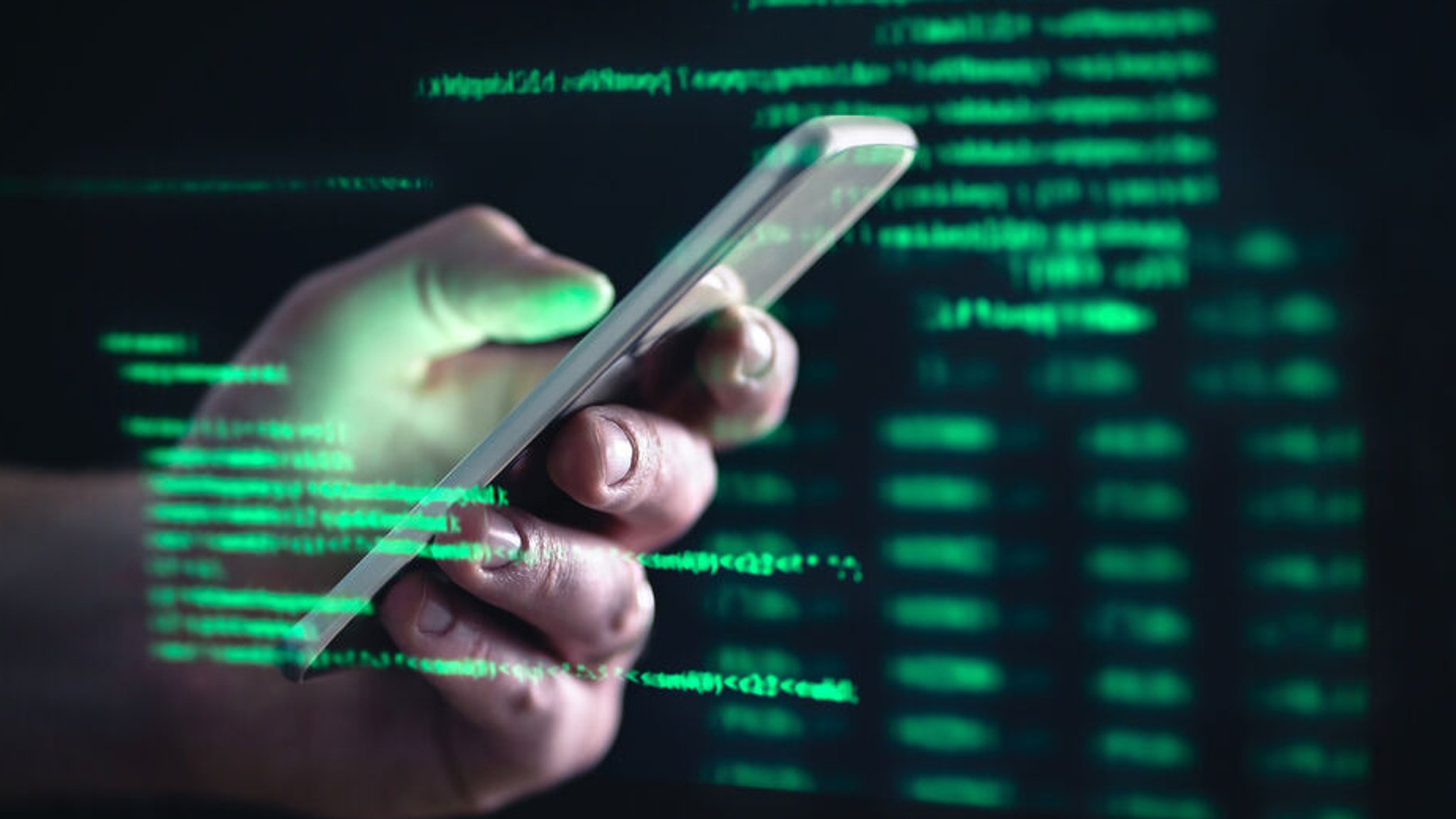 Eine Männerhand mit einem Smartphone in dunkler Umgebung mit leuchtend grünen Computercodes.