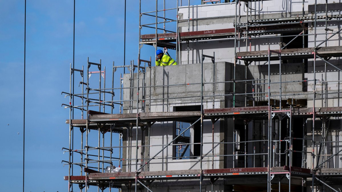 Ein Bauarbeiter steht auf einem Balkon auf einer Baustelle von einem neu gebauten Wohnhaus