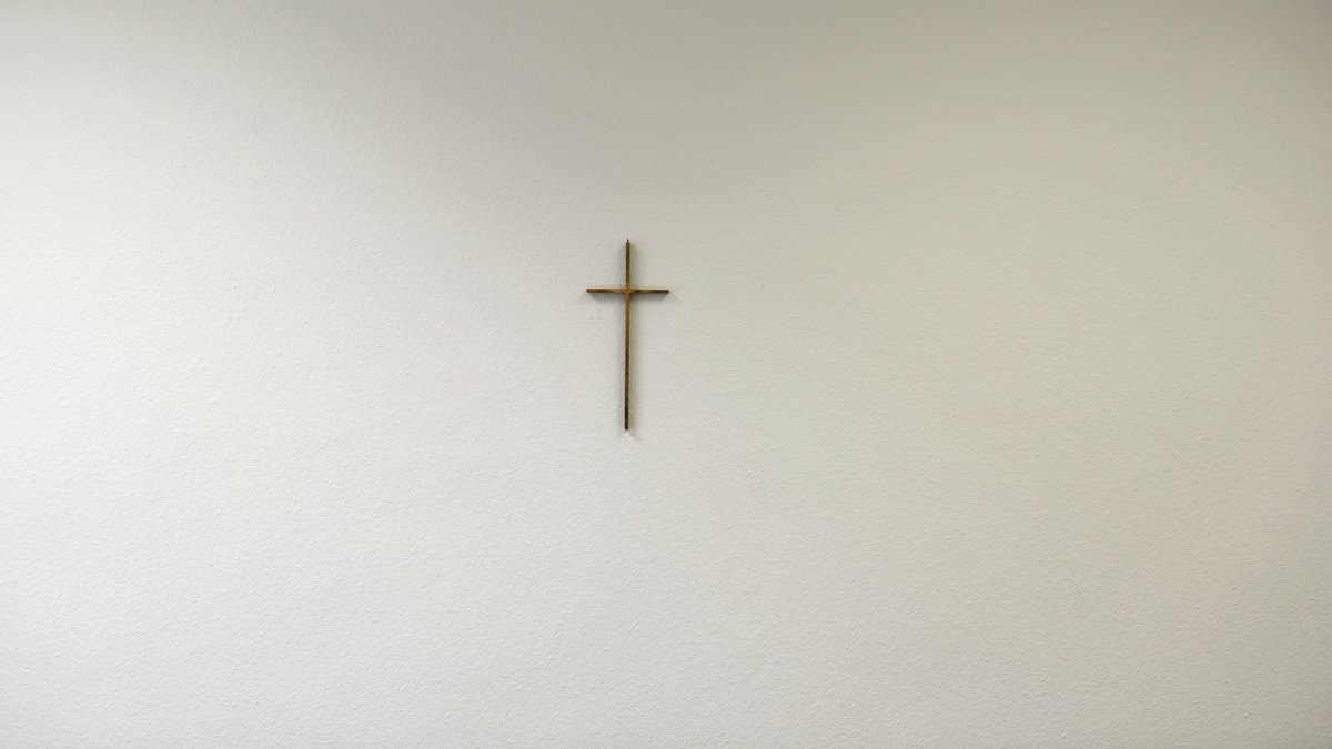 Ein schlichtes Metall-Kreuz auf einer ansonsten kahlen weißen Wand (Symbolbild)