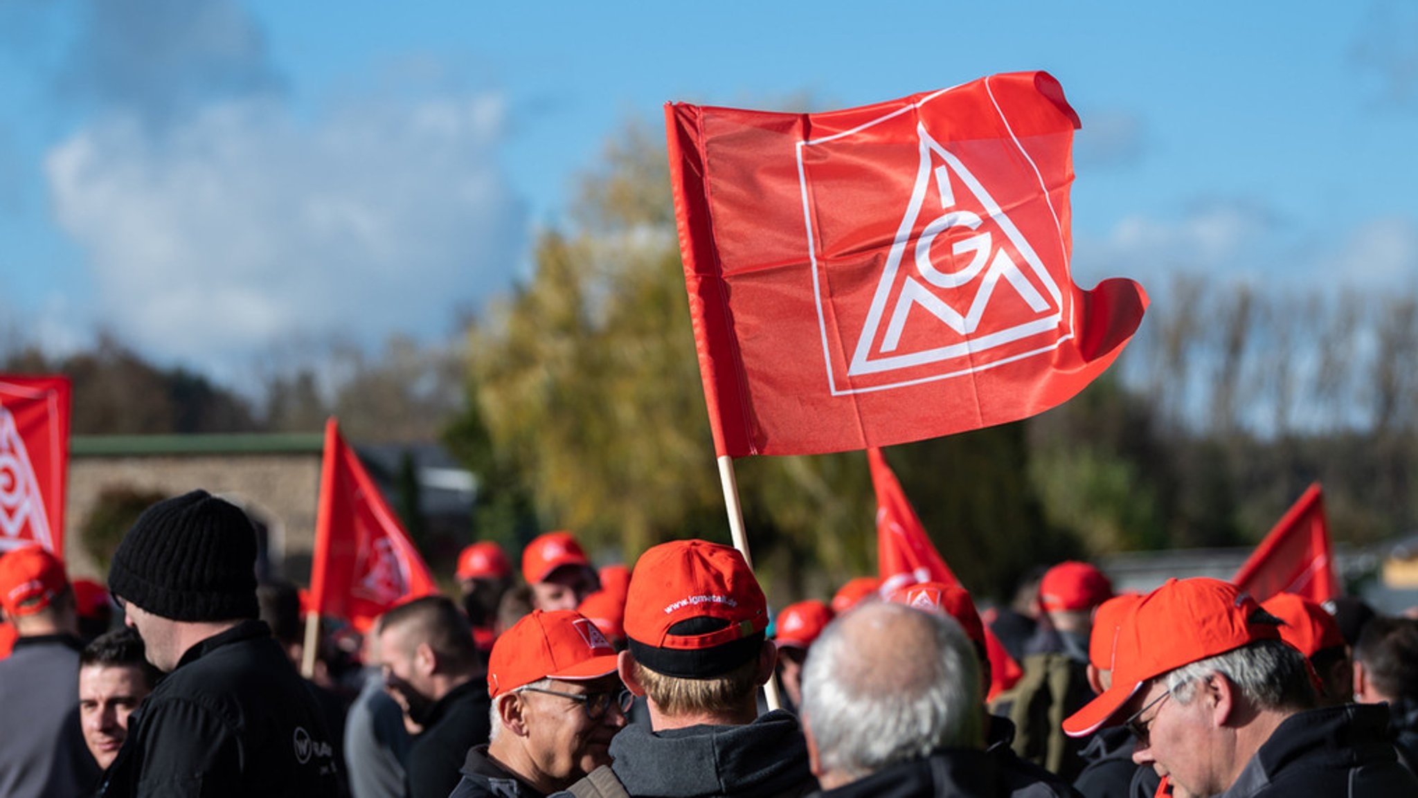 Arbeitnehmer streiken und tragen Mützen und Fahnen mit IG Metall Logo.