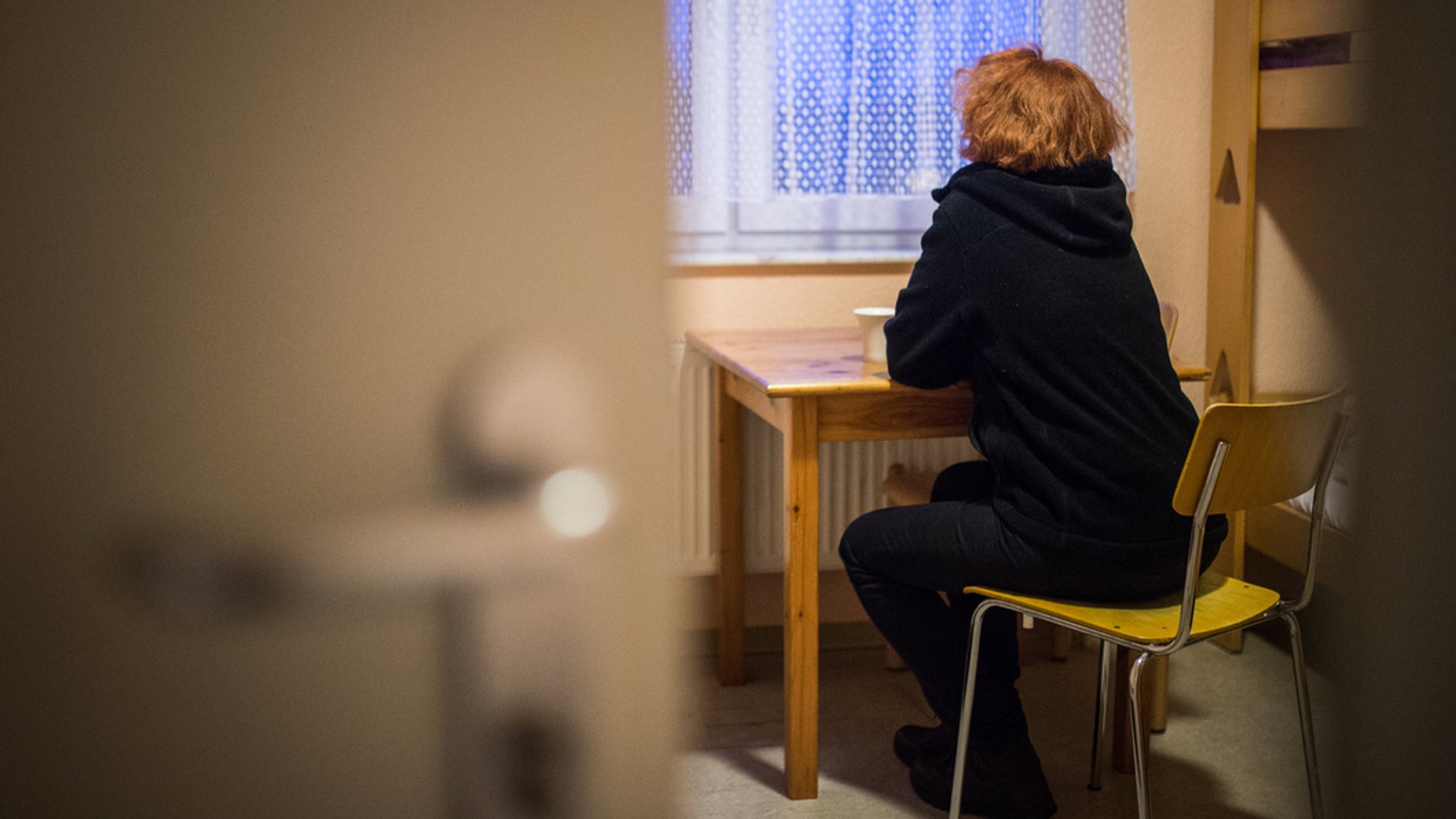 Eine Frau sitzt in einem Zimmer im Frauenhaus und schaut aus dem Fenster.