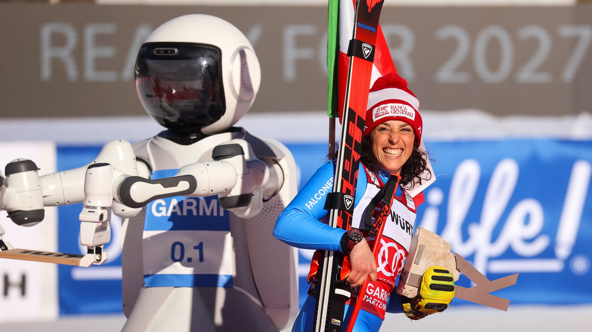 Die lachende Sportlerin steht neben dem etwas größer erscheinenden Roboter Garmi.