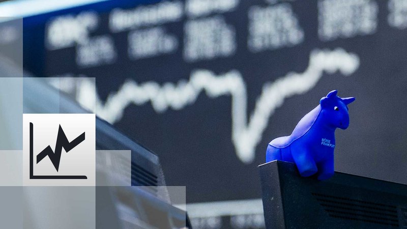 ein blauer Stieraus Gummi sitzt auf der oberen Kante eines Bildschirmes, im Hintergrund die Kurstafel der Börse