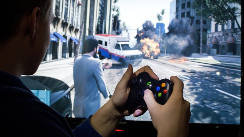 Ein  junger Mann sitzt vor einem Bildschirm und spielt "Grand Theft Auto V".