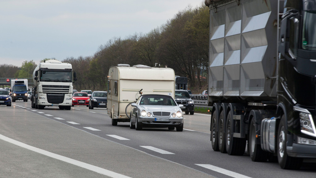 Fließender Verkehr auf der Autobahn A99 Richtung Nürnberg, darunter ist ein Auto mit Wohnanhänger zu sehen.