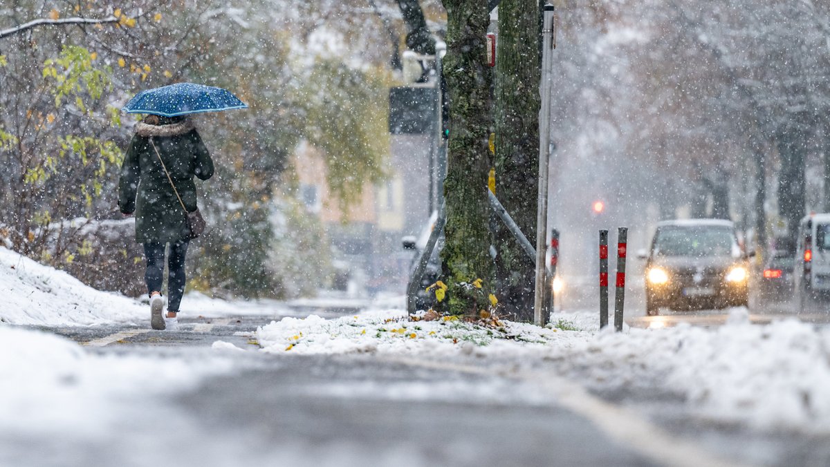 Eine Frau geht mit einem Regenschirm auf einem verschneiten Weg entlang. 