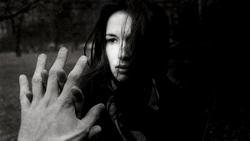 Auf einem Schwarz-Weiß-Foto sieht man eine Frau, die mit ihrer Hand eine andere Hand berührt, die ins Bild ragt. 