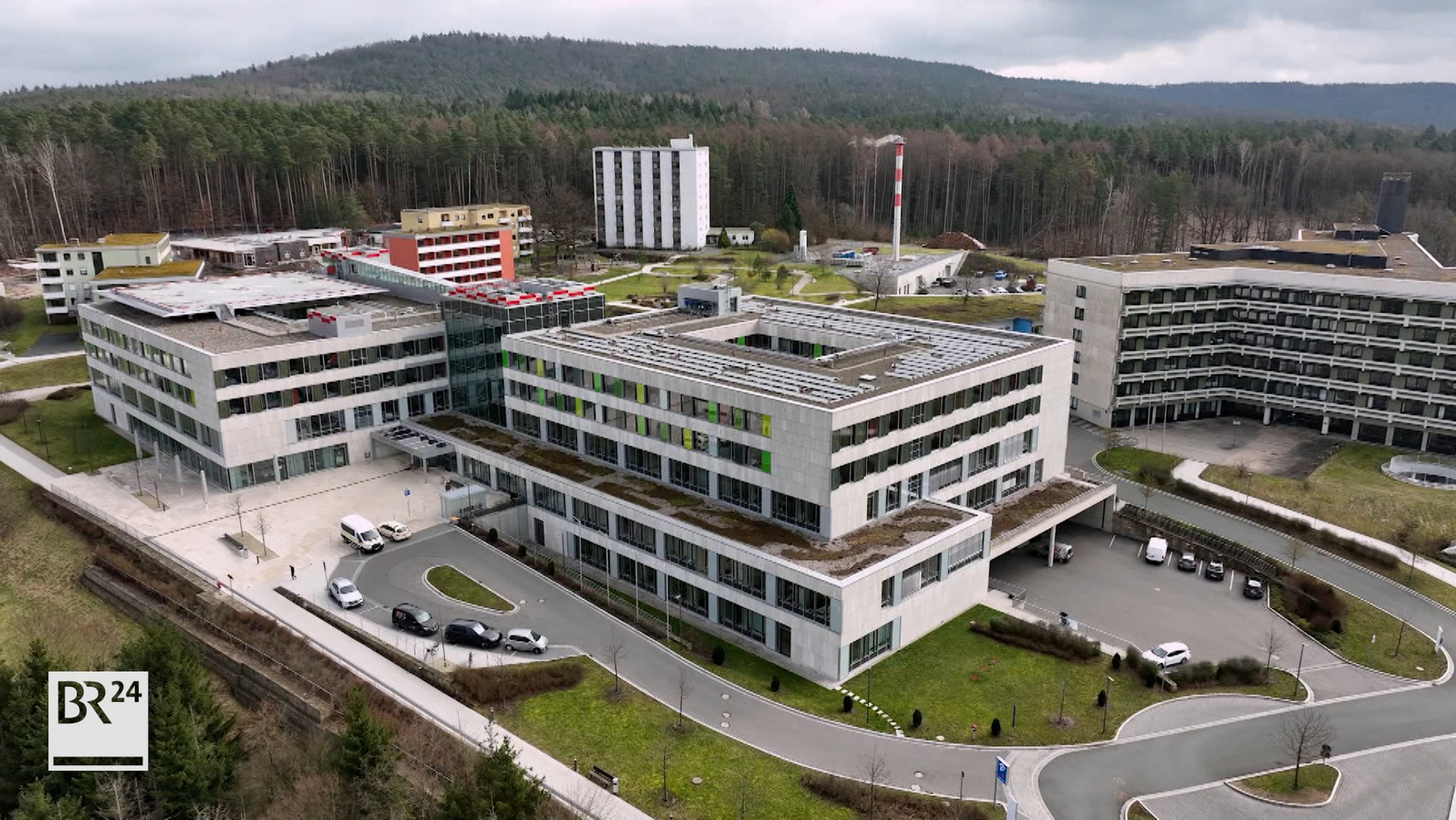 Blick auf mehrere Betongebäude, im Hintergrund Wald.