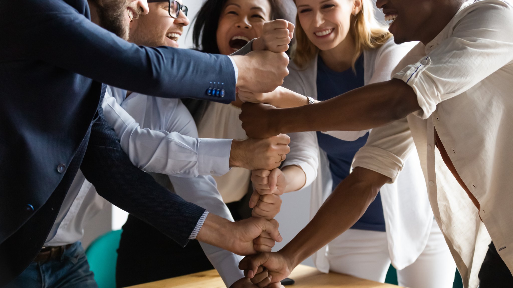 Ein Team aus Arbeitskollegen steht um einen Tisch im Kreis und legt die Fäuste übereinander.