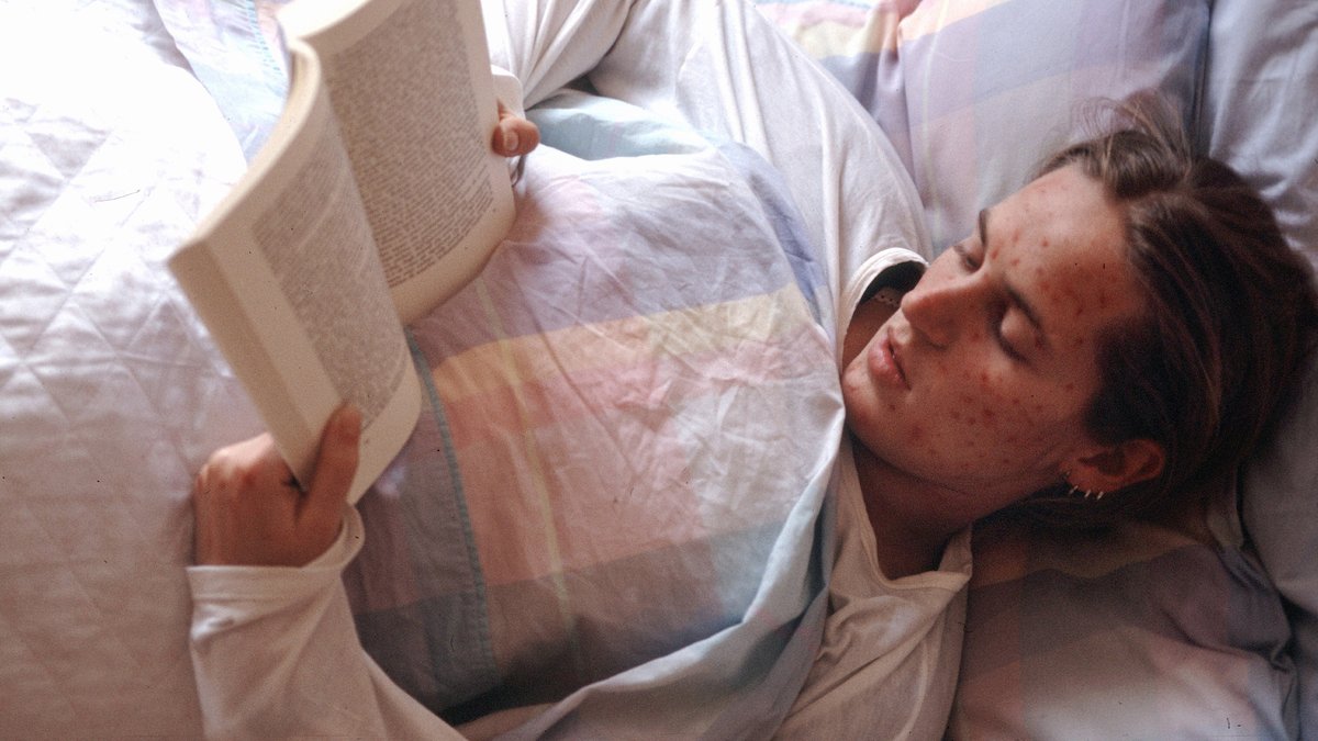 Eine Person liegt mit Masern im Bett und liest 
