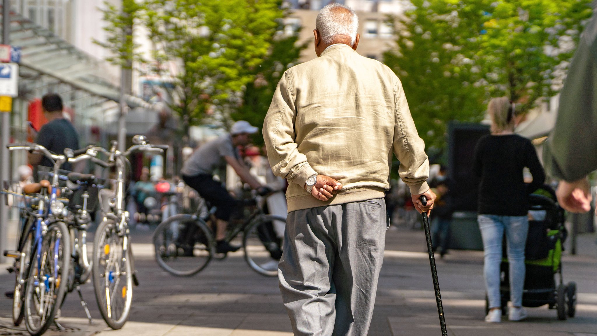 Ein älterer Herr mit Stock geht im Sonnenschein ruhigen Schrittes die Offenbacher Fußgängerzone entlang. 