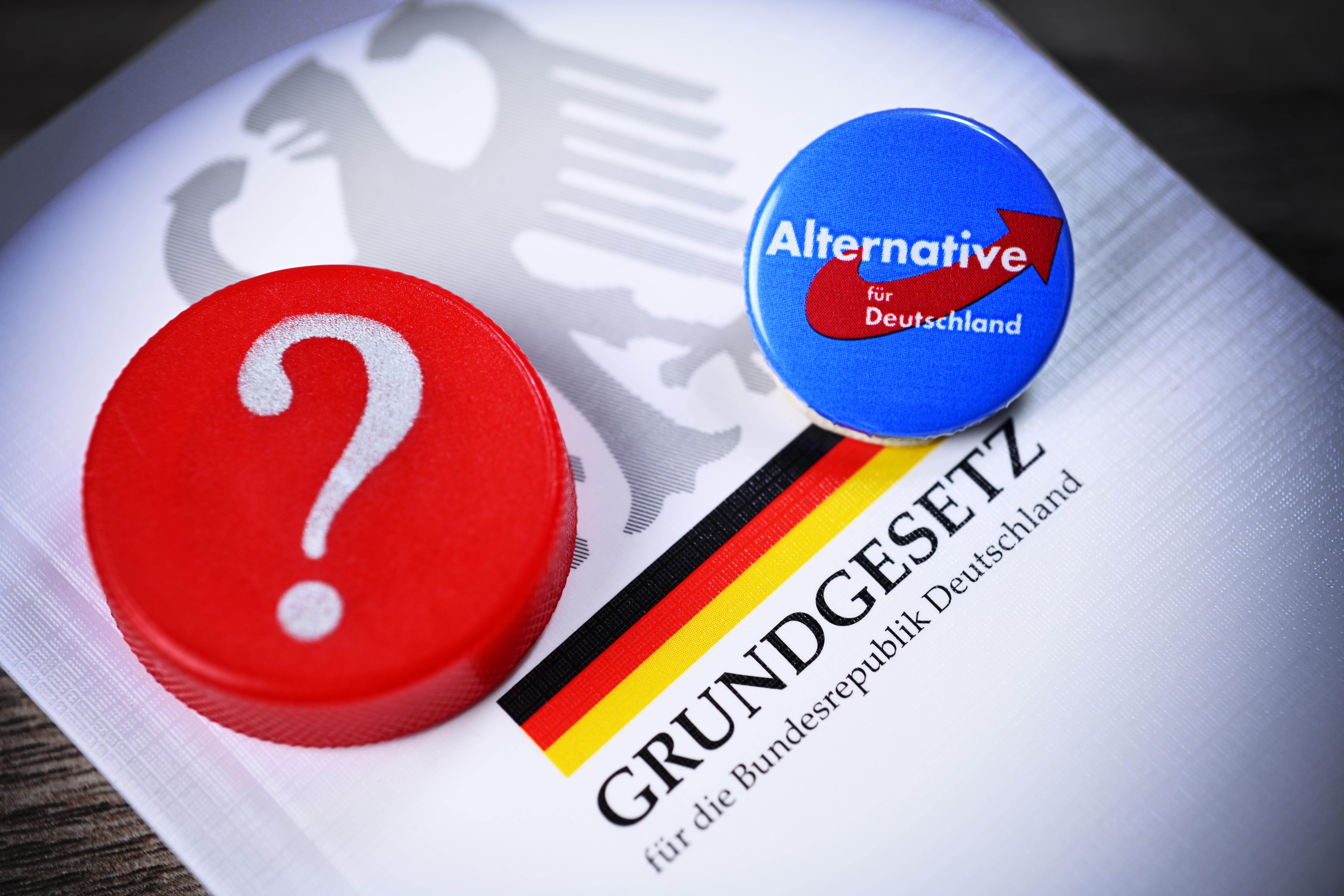 Parteianstecker der AfD und Fragezeichen auf dem deutschen Grundgesetz (Symbolbild)