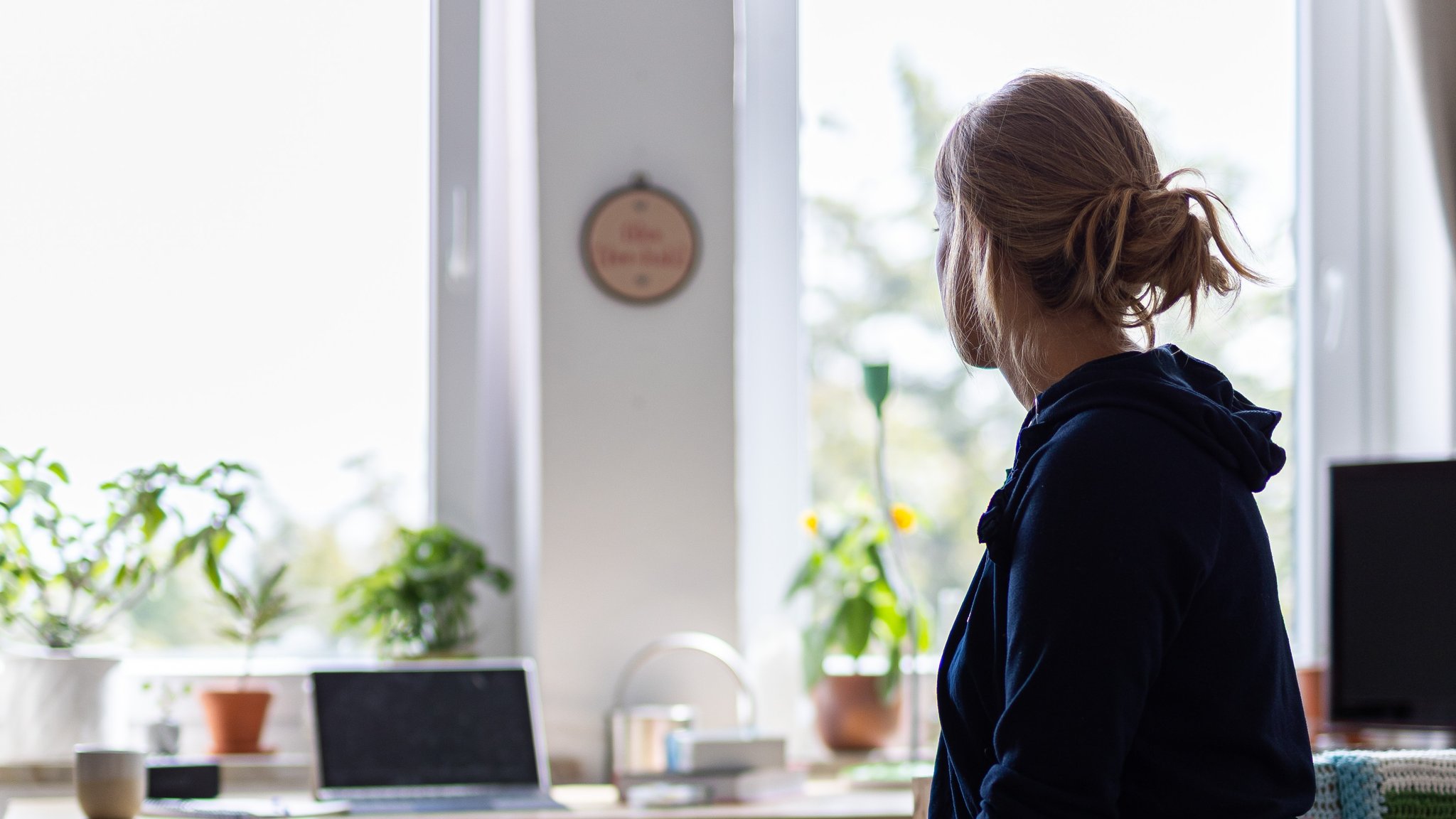 Eine Frau sitzt alleine in einem Zimmer und blickt aus dem Fenster.