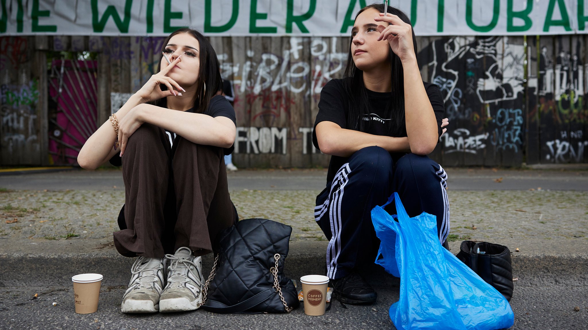 Symbolbild: Zwei junge Frauen sitzen gedankenverloren auf der Straße und rauchen.