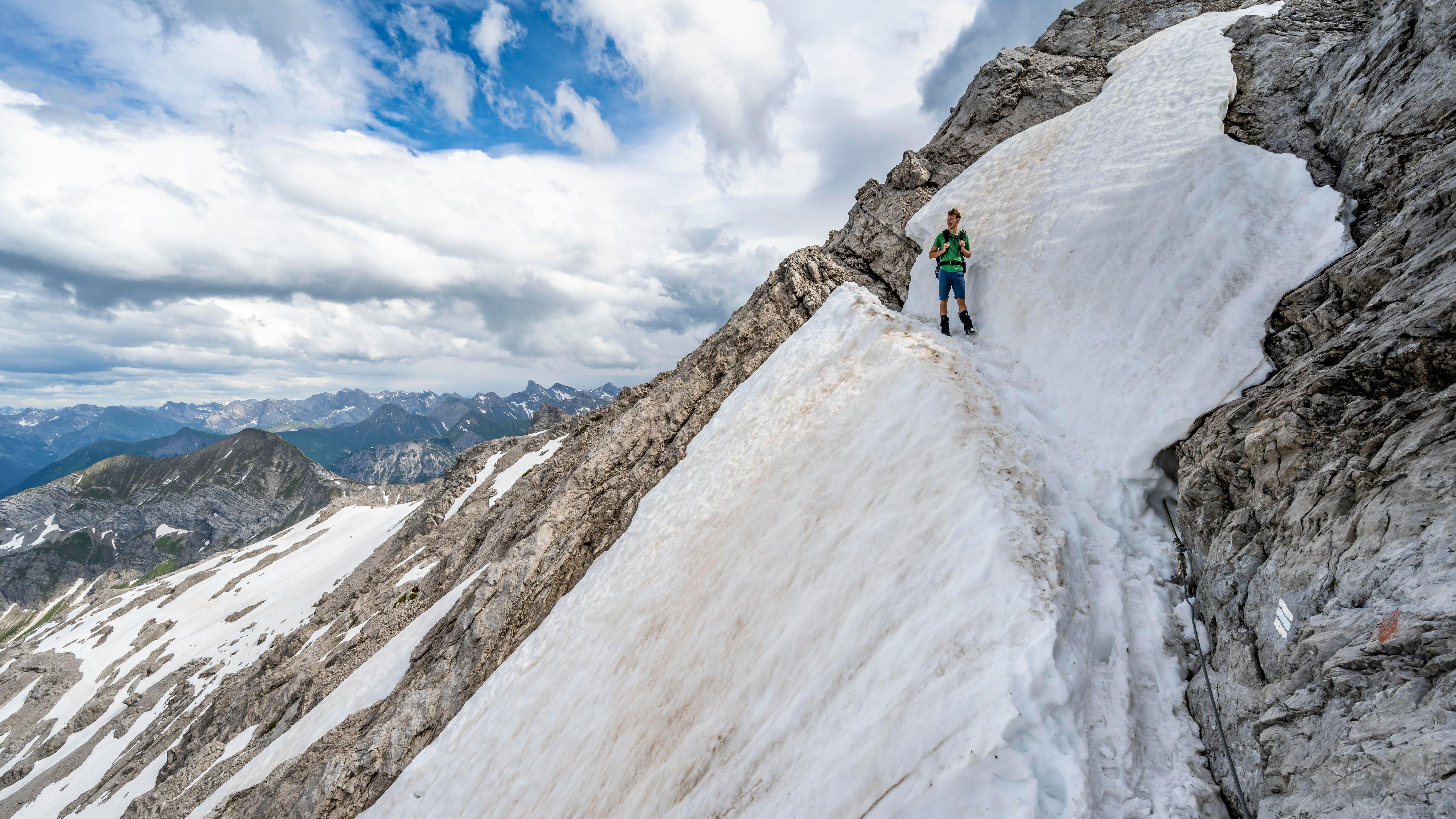 Wanderer im steilen Felsgelände mit Altschneefeldern.