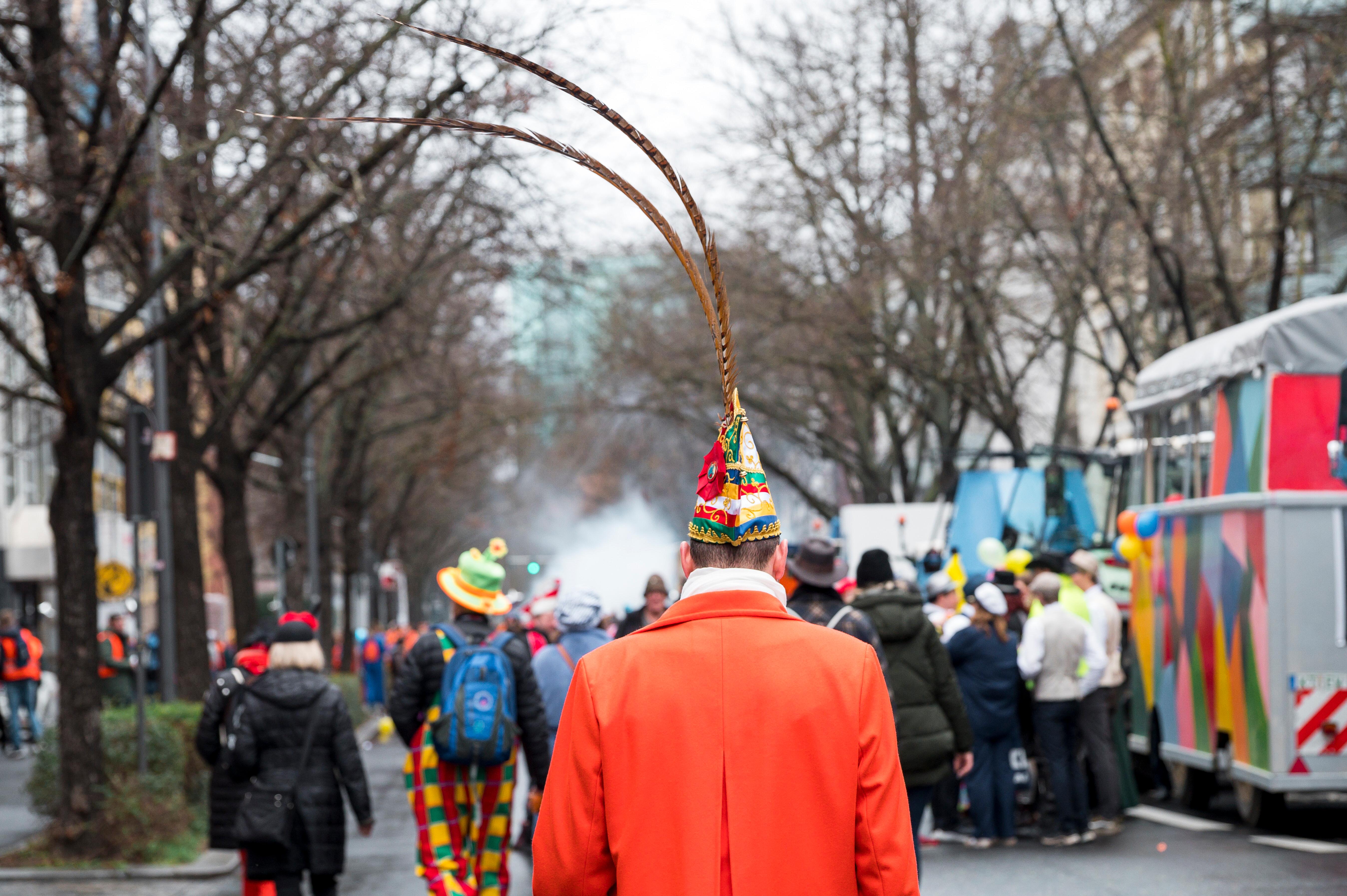 (Archivbild) Eine Narr mit Narrenkappe geht an Faschingswägen vorbei.