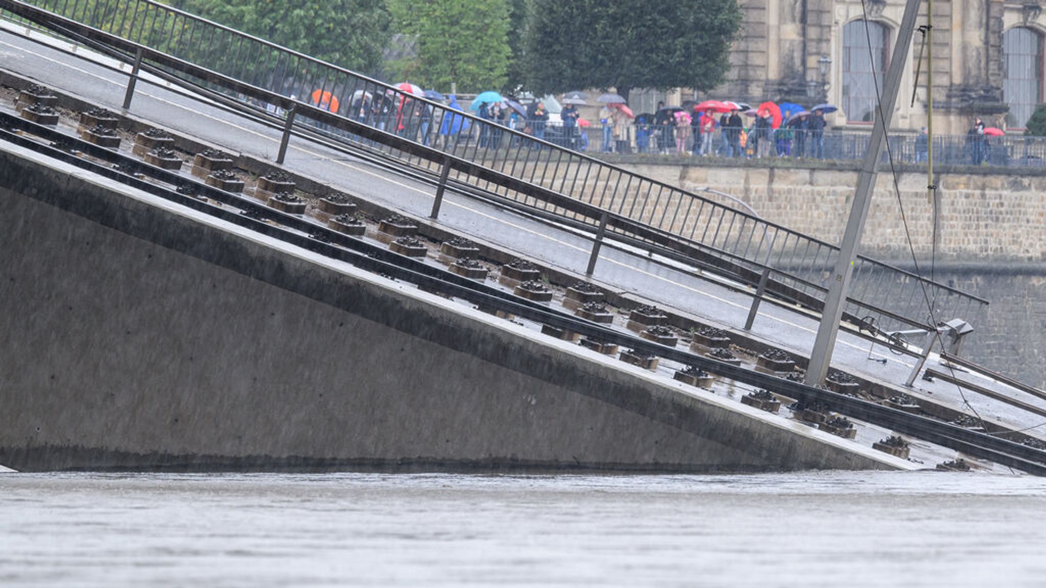 Wasser der Elbe fließt über Brückenteile der teilweise eingestürzten Carolabrücke, im Hintergrund sind Schaulustige auf der Brühlschen Terrasse zu sehen.