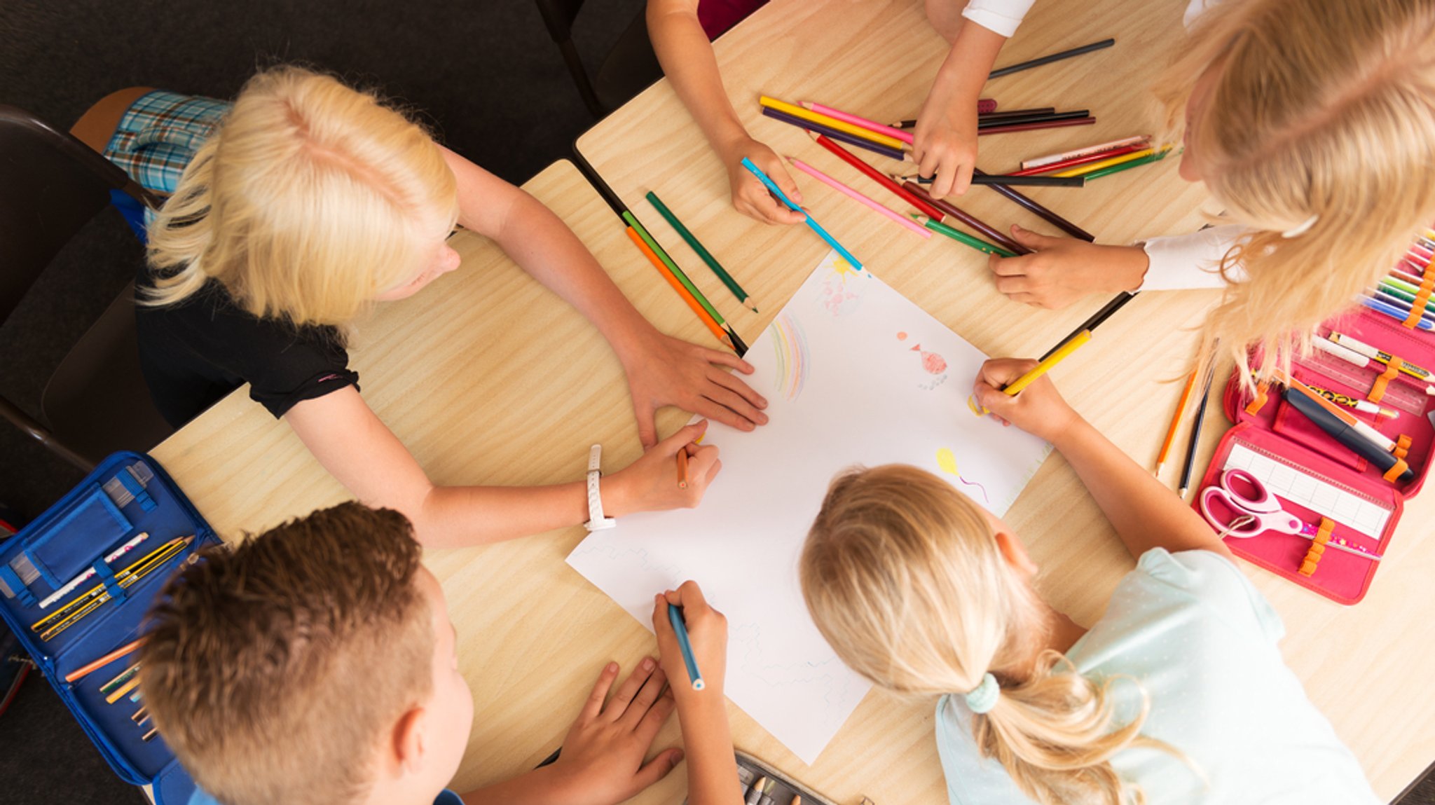 Grundschulkinder an einem großen Tisch malen gemeinsam.