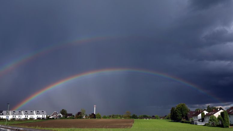 Ein doppelter Regenbogen spannt sich über Wohnhäuser und Ackerflächen. | Bild:picture alliance/dpa | Karl-Josef Hildenbrand