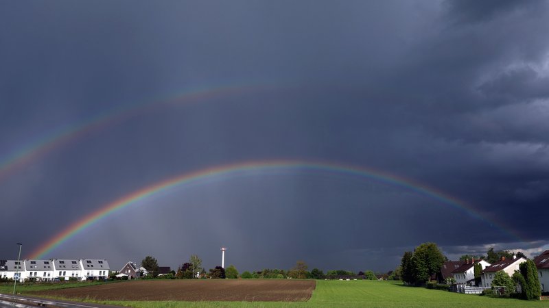 Ein doppelter Regenbogen spannt sich über Wohnhäuser und Ackerflächen.