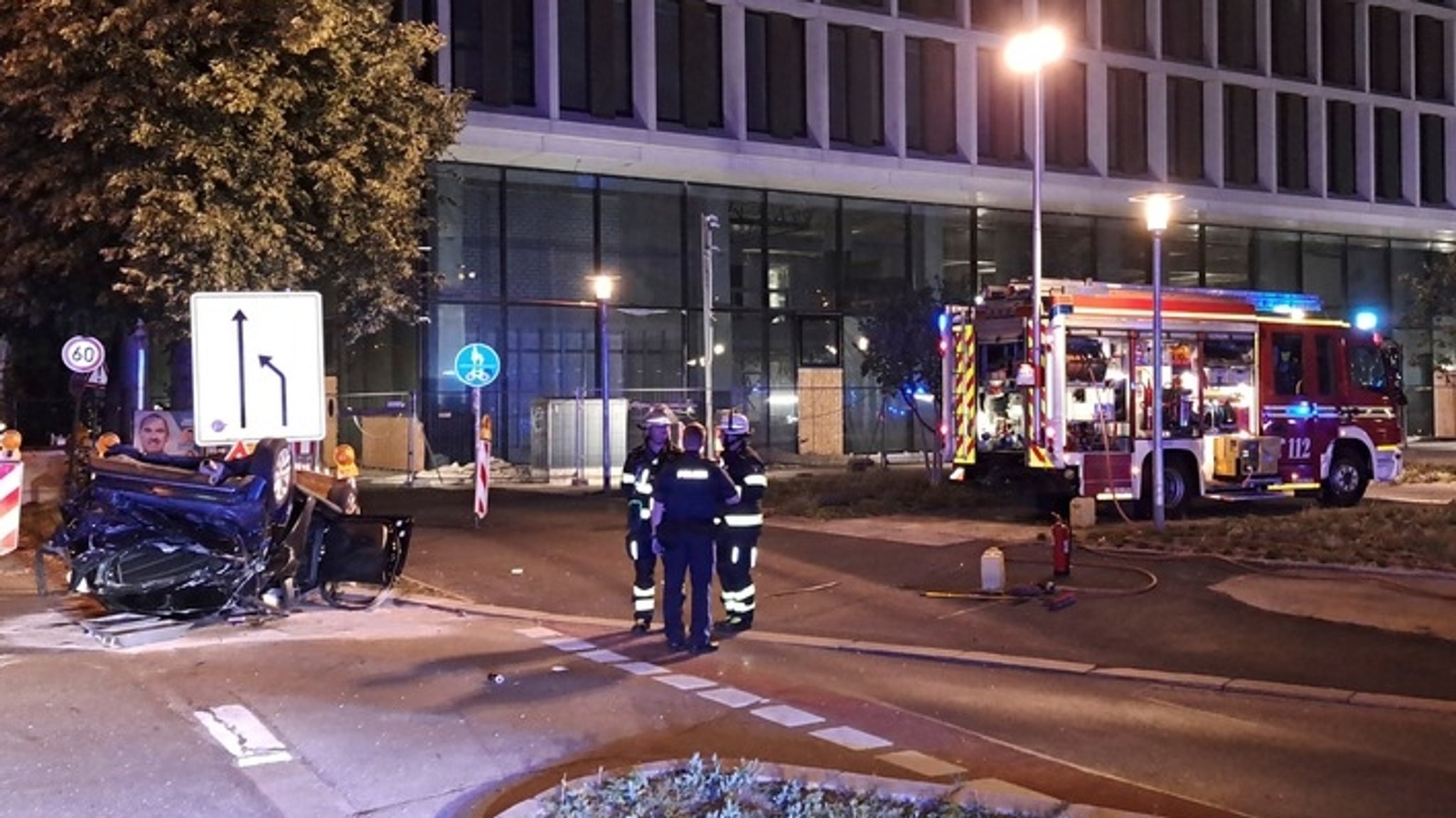 Feuerwehrleute stehen neben einem völlig zerstörten Kleinwagen, der auf dem Dach liegt.