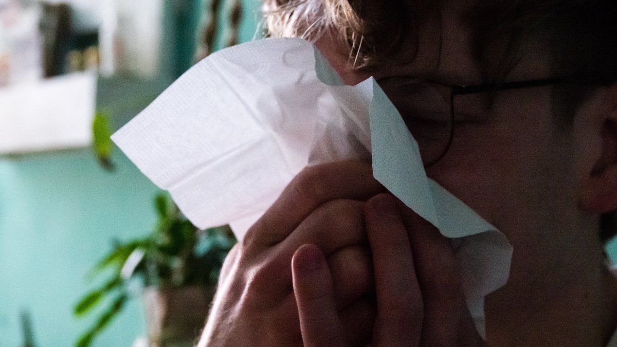 Ein Mann mit Taschentuch schnäuzt sich die Nase. 