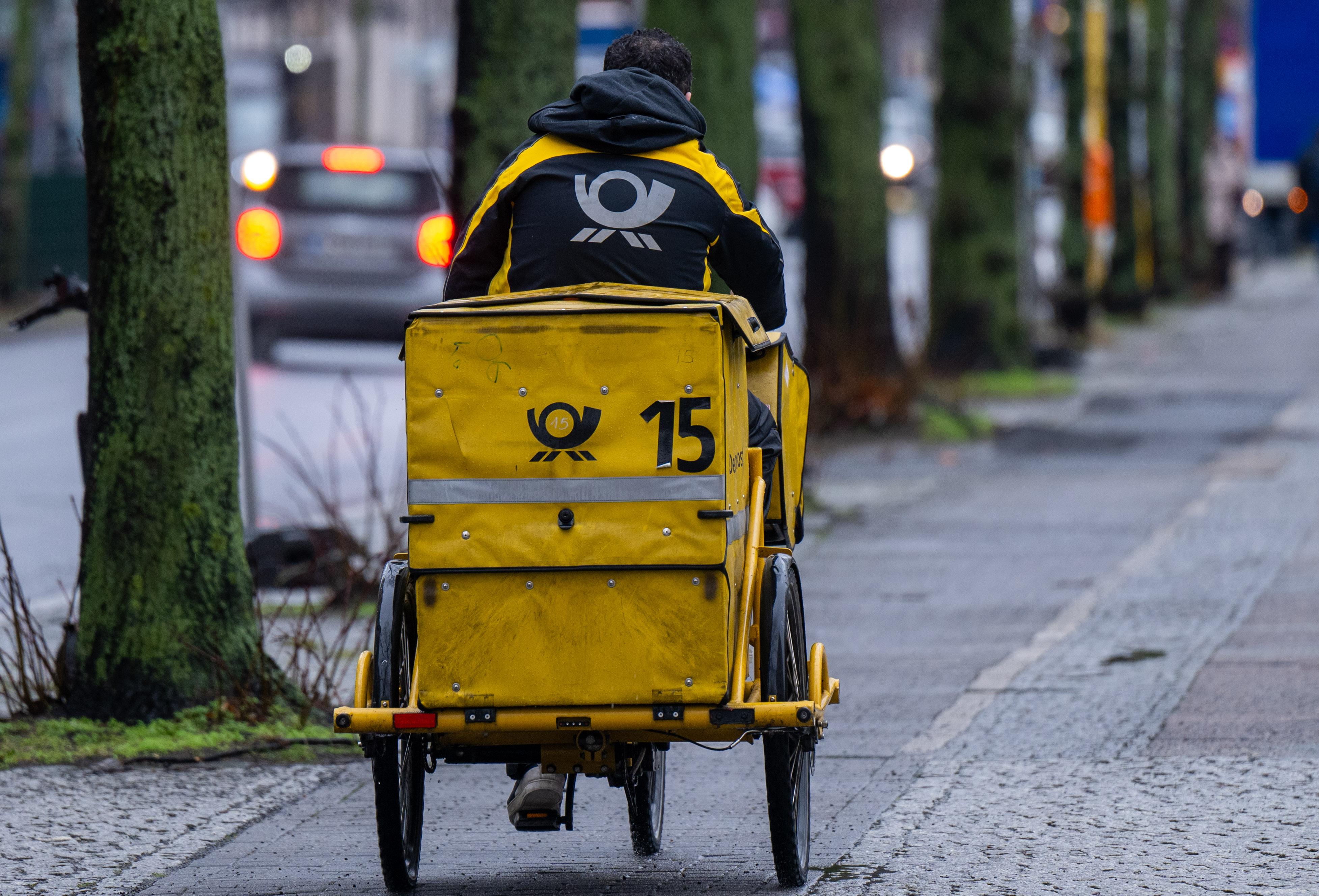 Ein Briefträger fährt mit seinem Fahrrad eine Straße entlang