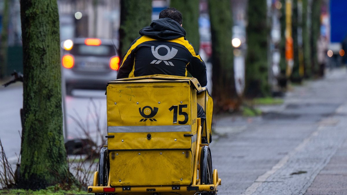 Ein Briefträger fährt mit seinem Fahrrad eine Straße entlang