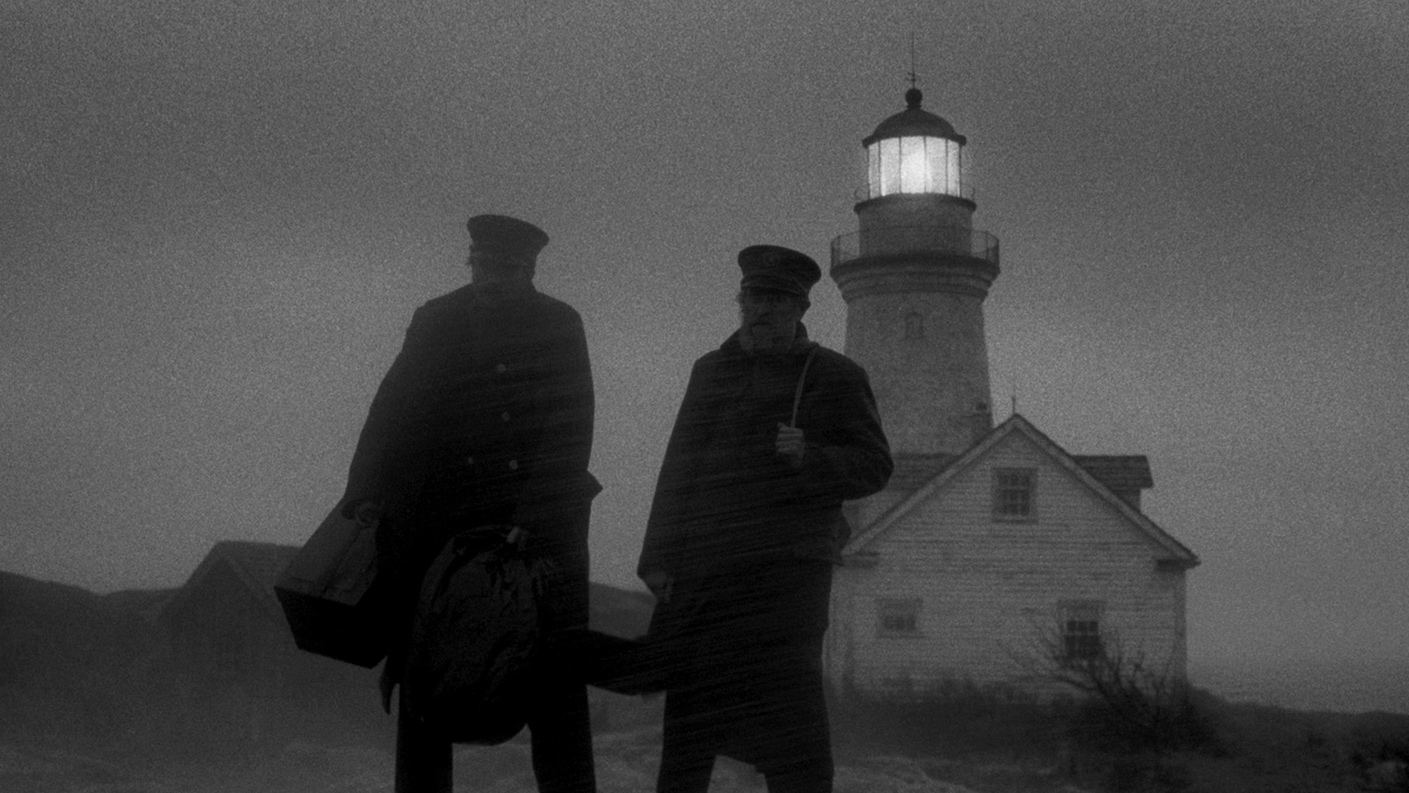 Zwei Männer in Uniform tragen schwere Koffer durch den Regen. Hinter ihnen steht ein Leuchtturm.