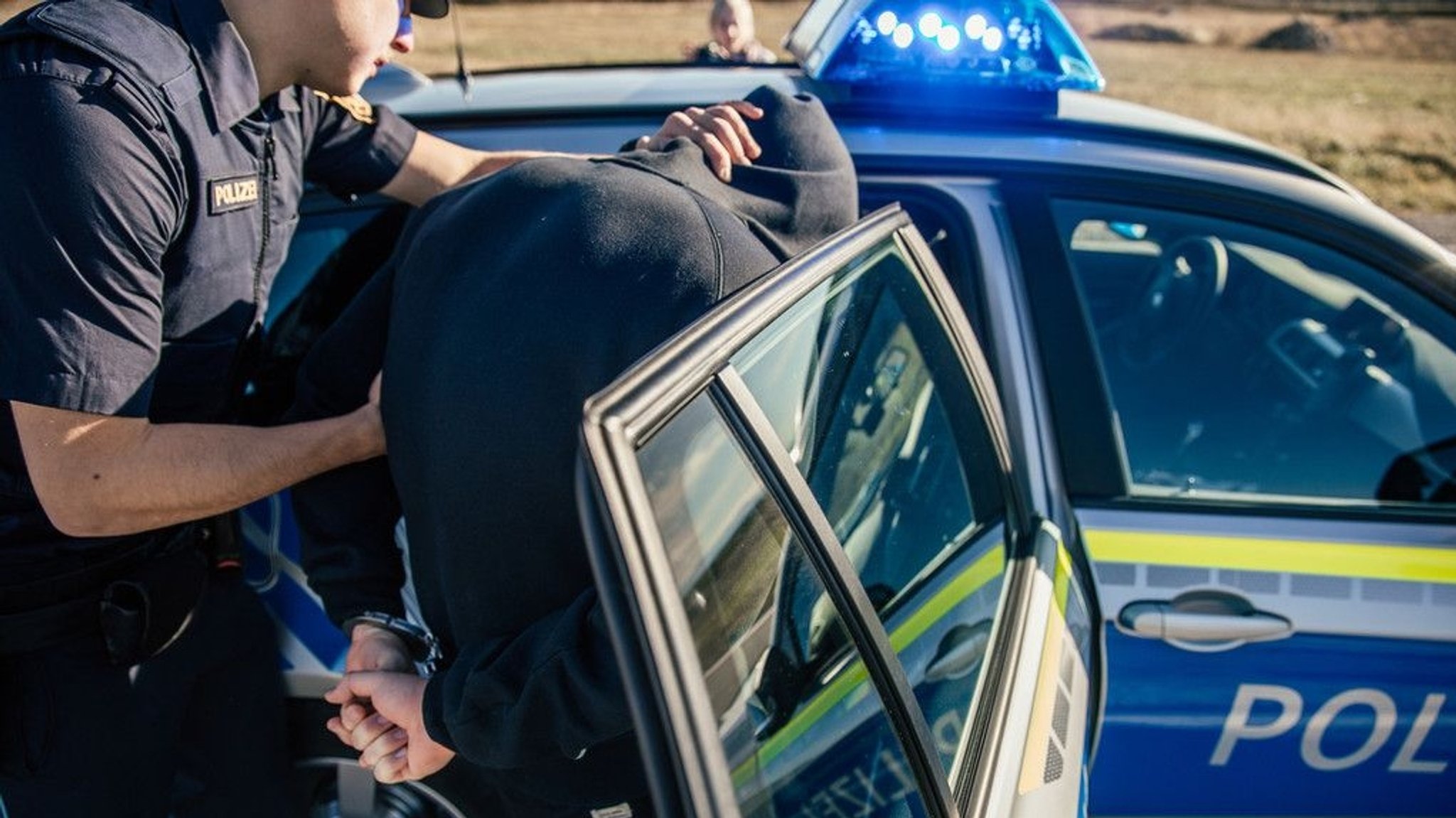 Symbolbild: Ein Polizist nimmt einen Mann fest und bringt ihn ins Polizeiauto.