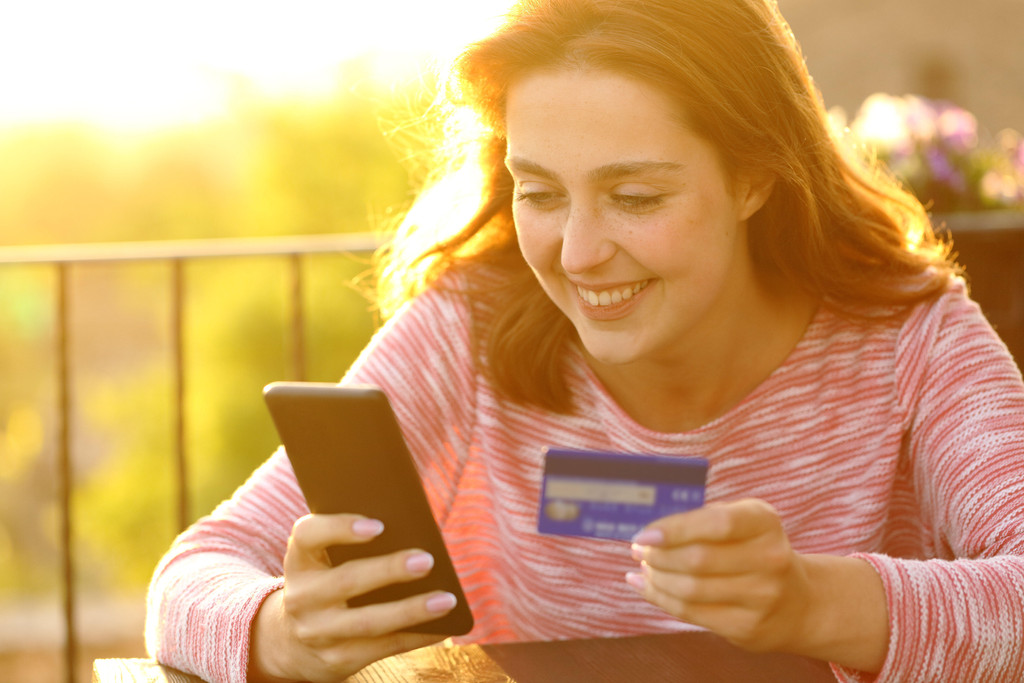 Eine Frau hält ein Handy und eine Kreditkarte in der Hand. Was ist das richtige Zahlungsmittel im Urlaub? (Symbolbild)