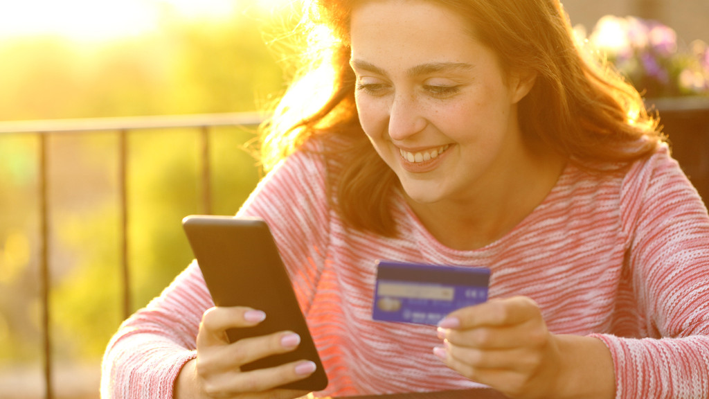 Eine Frau hält ein Handy und eine Kreditkarte in der Hand. Was ist das richtige Zahlungsmittel im Urlaub? (Symbolbild)