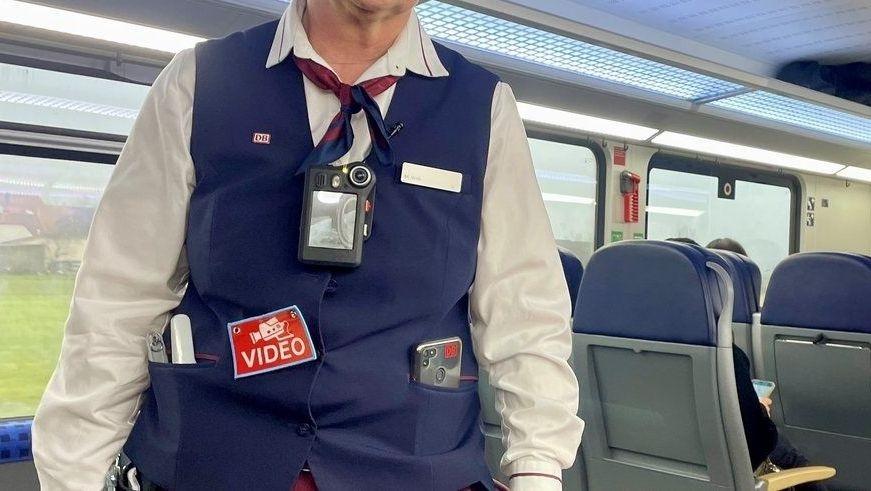 Eine Zugbegleiterin der Bahn in blauer Uniform trägt eine Bodycam am Oberkörper.