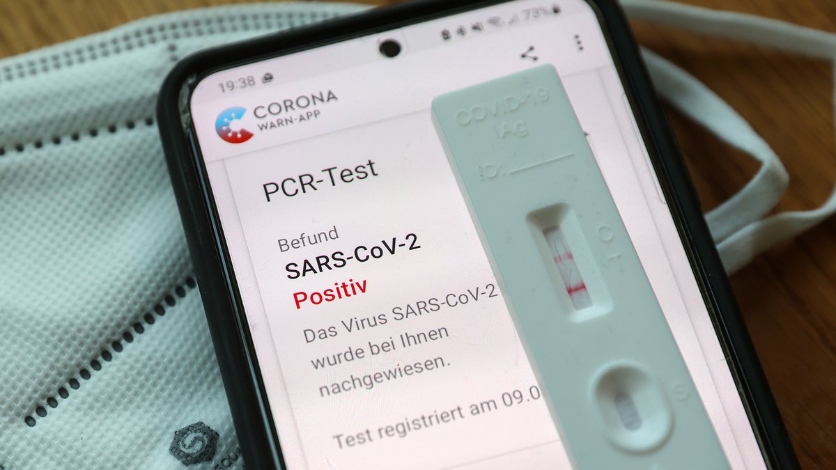Ein positiver Schnelltest liegt auf einem Handy, auf dem in der Corona-Warn-App ein positiver PCR-Test angezeigt wird (Symbolbild).