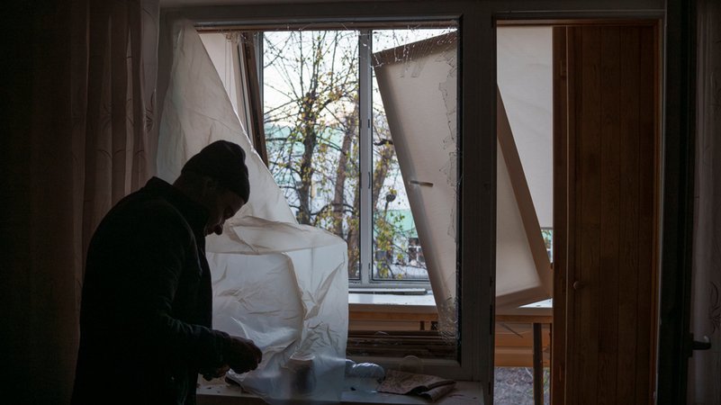 Ein Mann deckt ein zerbrochenes Fenster in seiner Wohnung in Kiew nach einem russischen Drohnenangriff mit Plastik ab. 