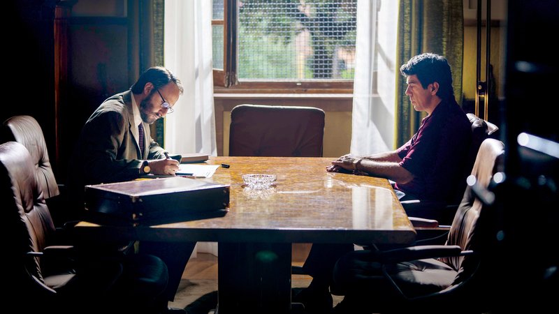 Zwei Männer sitzen an einem Besprechungstisch in einem dusteren Raum: Szene aus "Il Traditore"