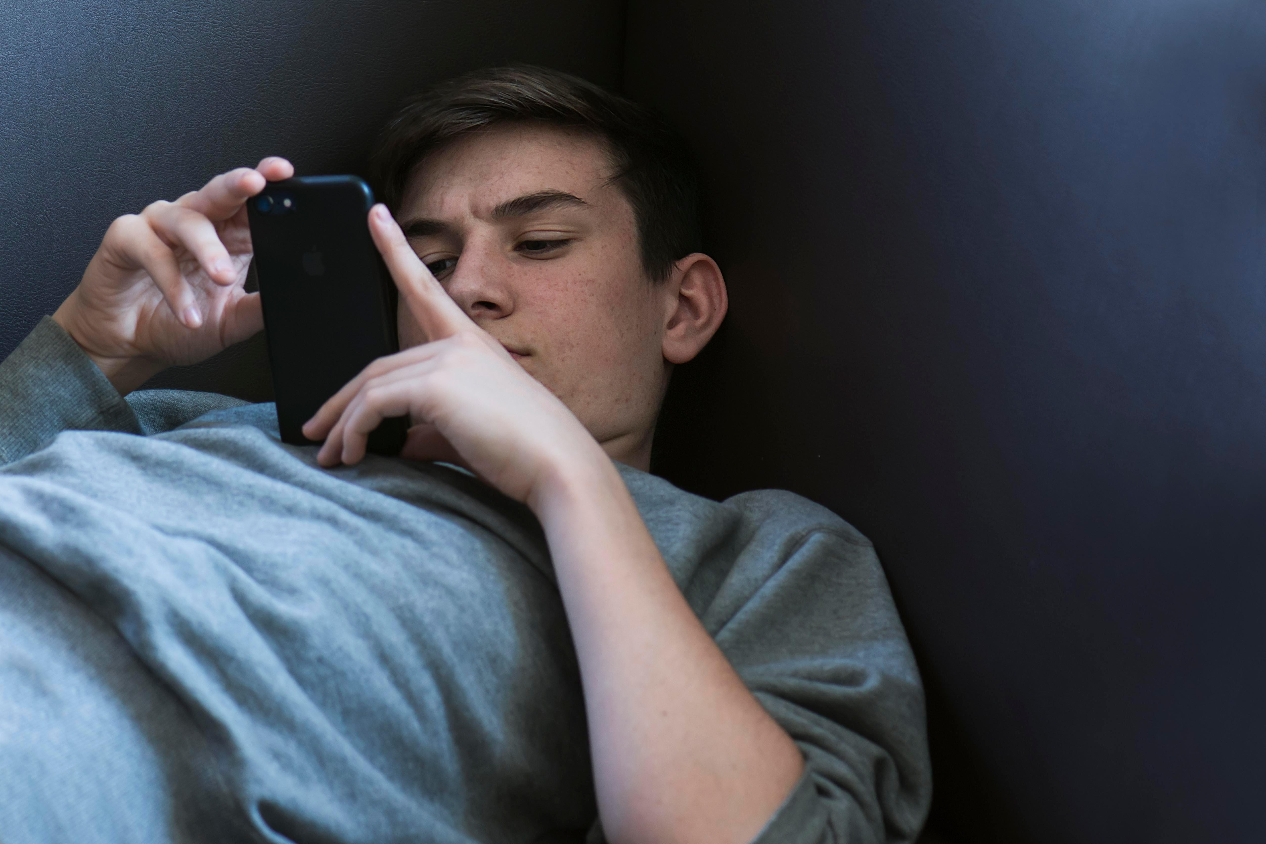 Jugendlicher liegt auf dem Sofa und spielt seinem iPhone