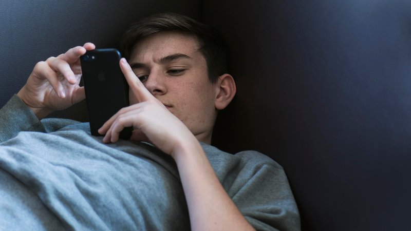 Jugendlicher liegt auf dem Sofa und spielt seinem iPhone