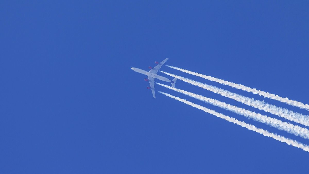 Kondensstreifen aus Triebwerksabgasen, cirrus aviaticus, die sich hinter einem viermotorigen Flugzeug vom Typ Airbus A340 am blauen Himmel bilden (Symbolbild)
